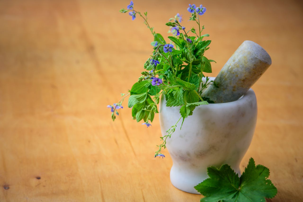 home-hero Marble mortar and pestle with fresh herbs and flowers on wooden table enhancing natural health and cooking aesthetics.